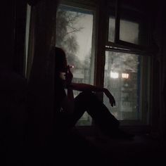 a woman sitting in front of a window while talking on a cell phone at night