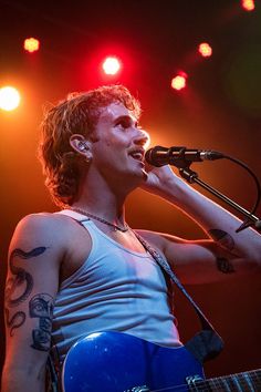 a man holding a blue guitar while standing in front of a microphone and singing into a microphone