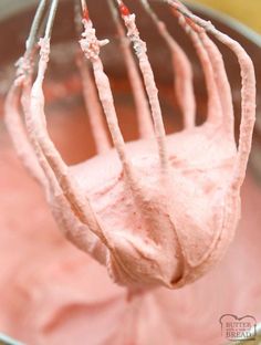 a whisk in a metal bowl filled with pink icing