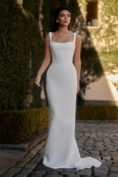 a woman in a white dress is standing on a brick walkway and looking off into the distance