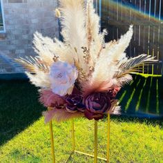 a vase filled with feathers and flowers on top of a metal stand in the grass