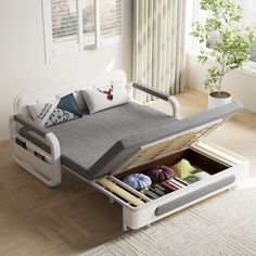 a white bed with drawers underneath it in a living room next to a large window