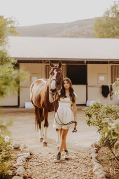 a woman walking with a horse in front of a barn