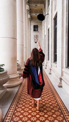 a woman is walking down the hallway with her graduation cap in hand and she is wearing a gown