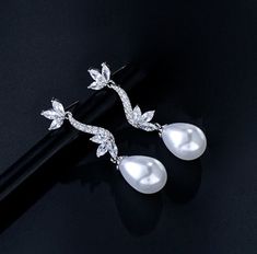 Romantic and elegant, this exquisite pair of earrings features iridescent white pearls and clear cubic zirconia that capture the light from every angle with a perfectly translucent appeal. The earrings are rhodium plated for a bright finish which enhances the intricate detailing and conveys a modern take on old elegance. Overall length of the earring is 38mm (approx. 1.5"). This exquisite design will add a touch of sophistication to any wedding gown or formal ensemble. Luxury Wedding Pearl Earrings With Lever Back, Luxury Pearl Earrings With Elegant Design For Formal Events, Luxury Pearl Bridal Earrings With Elegant Design, Luxury Elegant Pearl Earrings For Wedding, Luxury Elegant Pearl Bridal Earrings, Luxury White Feminine Earrings, Luxury Sterling Silver Elegant Pearl Earrings, Luxury Elegant Pearl Earrings In Sterling Silver, Luxury Timeless Cubic Zirconia Bridal Earrings