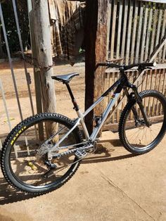 a mountain bike parked next to a wooden pole on the side of a road in front of a fence