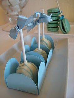 blue and white cake pops are in a row on a plate with cookies behind them