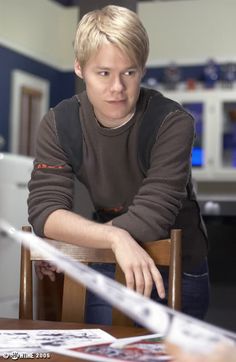 a young man sitting at a table in front of a laptop computer with his hand on the desk