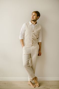 a man standing in front of a white wall with his hands on his hips wearing a vest and pants