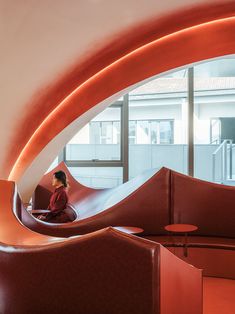 a woman sitting on top of a red bench next to a large window in a building