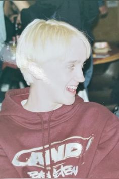 a young man with blonde hair wearing a red hoodie and smiling at the camera