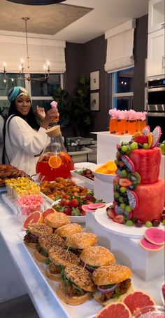 a woman standing in front of a buffet table filled with different types of sandwiches and fruit