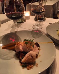 a white plate topped with food next to two glasses of wine on top of a table