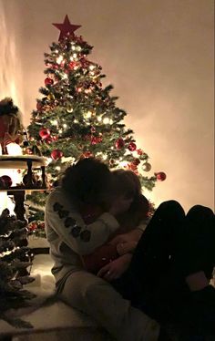 two people sitting next to each other in front of a christmas tree with lights on