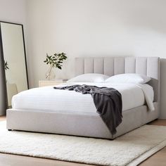 a white bed sitting on top of a wooden floor next to a tall dresser and mirror