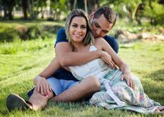 a man and woman sitting in the grass hugging each other with trees in the background