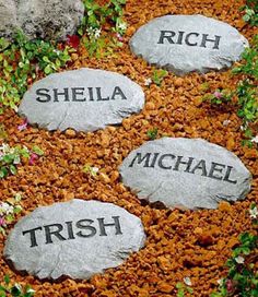 three stone steppings with names on them in the ground next to flowers and rocks