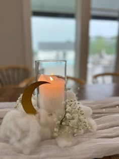 a candle and some flowers on a table with a window in the backround