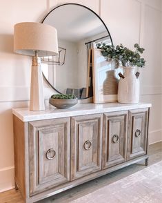 a mirror and some vases on top of a dresser next to a table with a lamp