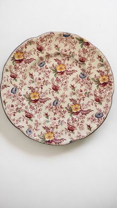 a plate with floral designs on it sitting on a white tableclothed surface, in the shape of a flower