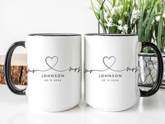 two personalized coffee mugs sitting on a table with flowers in the vase behind them