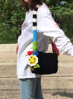 a woman is holding a black purse with a flower on the handle and a smiley face decoration hanging from it