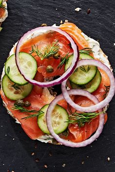 an open face sandwich with cucumbers, tomatoes and onions on it sitting on a black surface