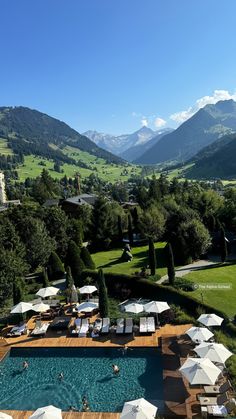 an outdoor swimming pool surrounded by mountains and greenery with umbrellas in the foreground