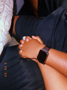 two people holding hands while sitting on the ground with an apple watch in their lap