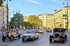 an old time car driving down the street in front of other cars and people onlookers