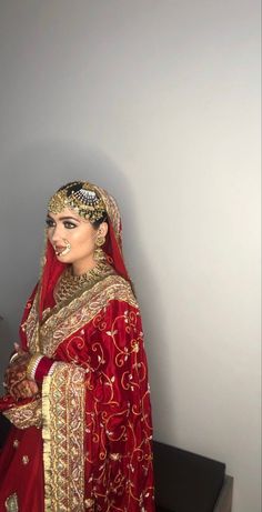 a woman in a red and gold bridal dress standing next to a white wall