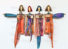 three dolls are hanging on the wall with scarves and umbrellas attached to them