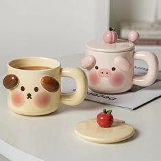 two coffee mugs sitting on top of a table next to a plate with an apple