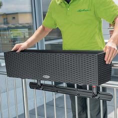 a man standing behind a metal fence holding onto a black piece of luggage that is attached to it