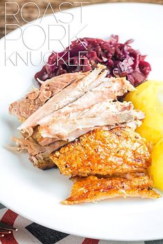 a white plate topped with meat and potatoes next to red cabbage on a checkered table cloth