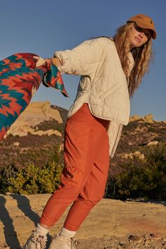 a woman is standing on top of a hill with a scarf in her hand and she is looking at the camera