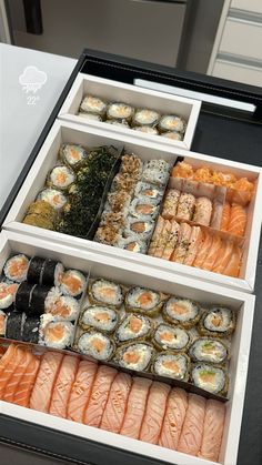 an assortment of sushi and other food items displayed in trays on a counter