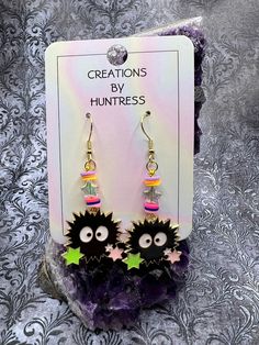 the earrings are decorated with black and yellow stars, pink and green beads, and an evil face