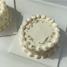 there is a white cake on the table next to another cake that has been decorated with seashells