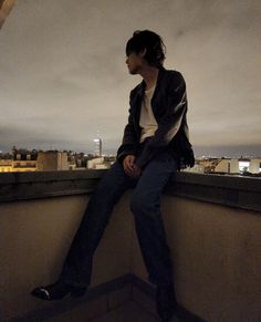 a man sitting on top of a roof next to a tall building with a city skyline in the background