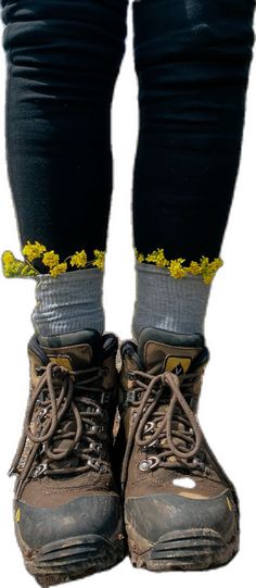 a pair of hiking boots with yellow flowers on the soles and black pants, standing next to a rock