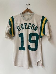 True vintage 1960's athletic Jersey. All cotton jersey with crunchy lettering, and a couple holes as per pictures. Total winner, this one is. Tag: Hanesport- Men's S 34/36 Fabric: 100% cotton Front: OREGON 19 Back: 19 PTP: 16 3/4", Length: 26 1/2", Sleeve: 11 1/2" No refunds, returns or exchanges. You have options in shipping. We will only ship outside of North America with tracking. Cotton Jersey For Streetwear With Team Spirit, Cotton Jersey For Streetwear During Sports Season, Throwback Cotton Tops For Sports Season, Cotton Jersey For Sports Season Streetwear, Retro Cotton Tops With Team Name, Cotton Jersey With Letter Print For Sports Season, Cotton Crew Neck Sports Jersey, Throwback Cotton Tops For Sports Events, Cotton Team Spirit Sports Jersey