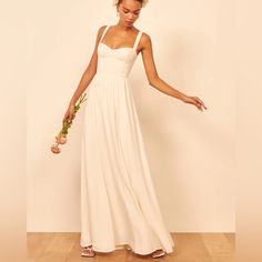 a woman in a white dress is holding flowers and looking down at the floor with her hand