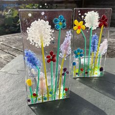 two glass vases with flowers in them sitting on a stone table top, one is made out of plastic and the other has colorful beads