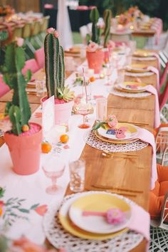 a long table with plates and cactus plants in pots on it's sides, along with place settings