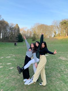 three young women are posing for the camera in a field with their arms up and legs spread out