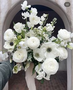 a white vase filled with lots of flowers on top of a brick floor next to an archway