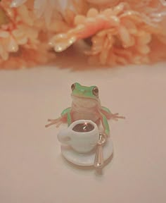 a tiny frog sitting on top of a white saucer next to a cup of coffee