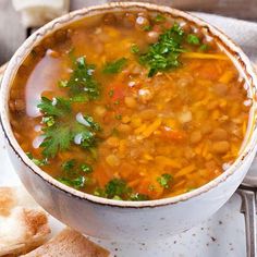 a white plate topped with a bowl of soup next to two pita breads