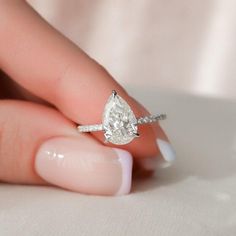 a woman's hand holding an engagement ring with a pear shaped diamond on it